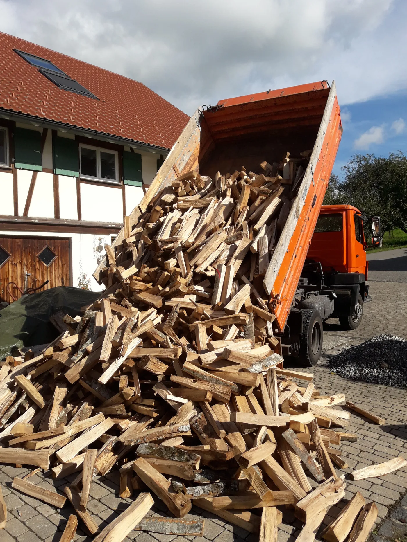 Brennholz wird bei einer Lieferung vom Kipper abgeladen